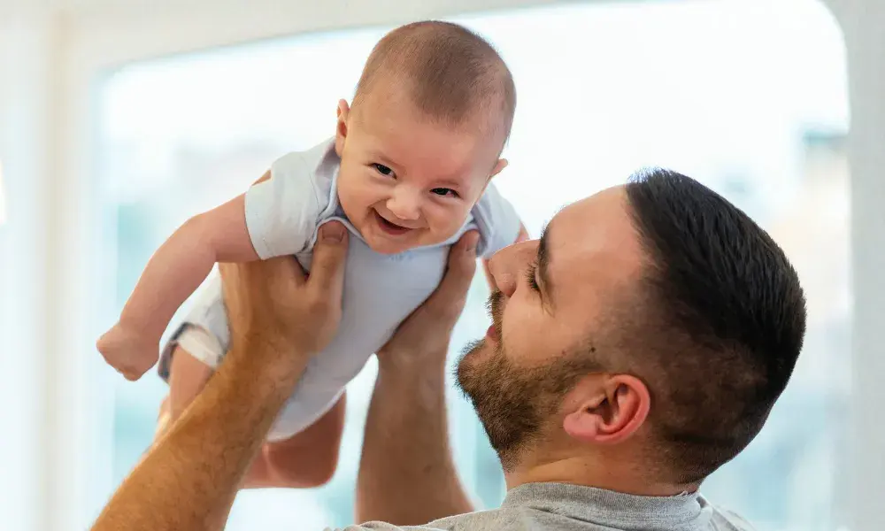 A dad or caregiver raises his baby son into the air