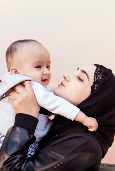 a woman wearing a hijab cradling her one year old