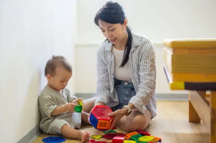 A young east asian mum plays with her two year old on a mat
